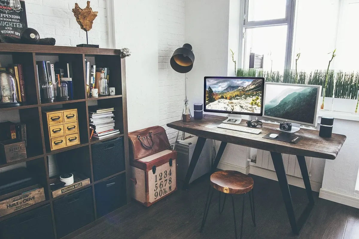 Modern home office desk with two monitors, a desk lamp, shelves and plants by a window