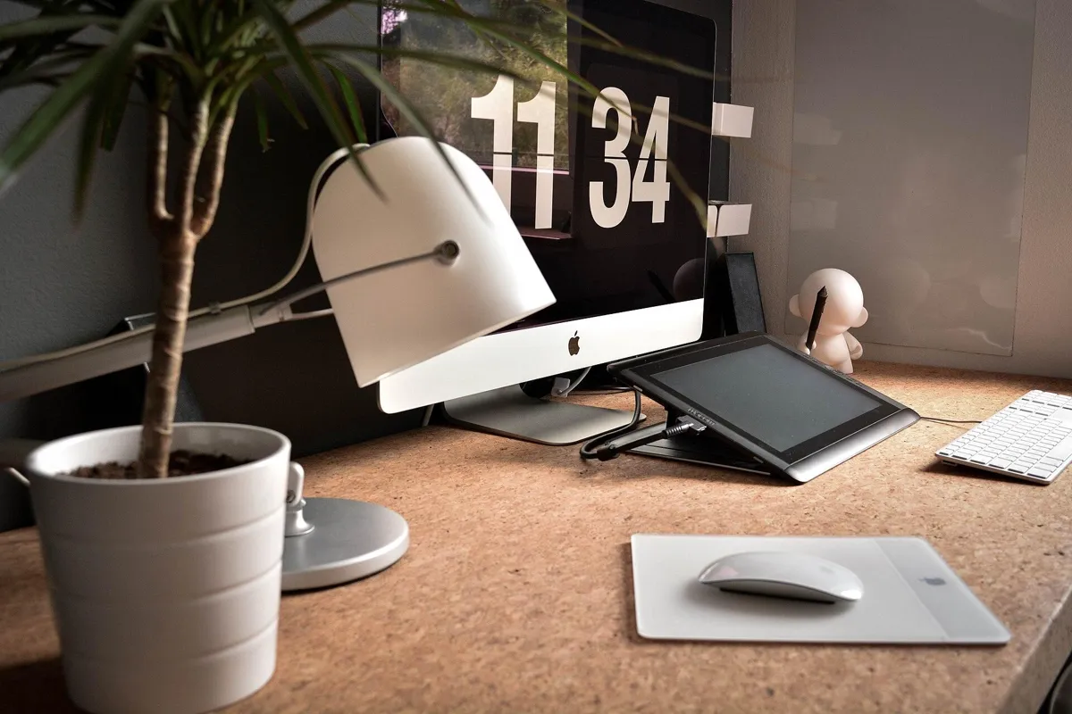 Minimal office desk with a monitor, white desk lamp, tablet and potted plant
